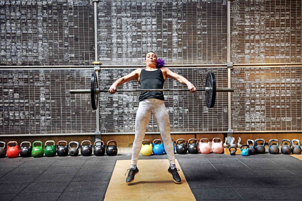 Woman athlete doing the snatch with a barbell snatching it off the ground to lift it above her head in a single movement seen straining with effort as she raises the weight