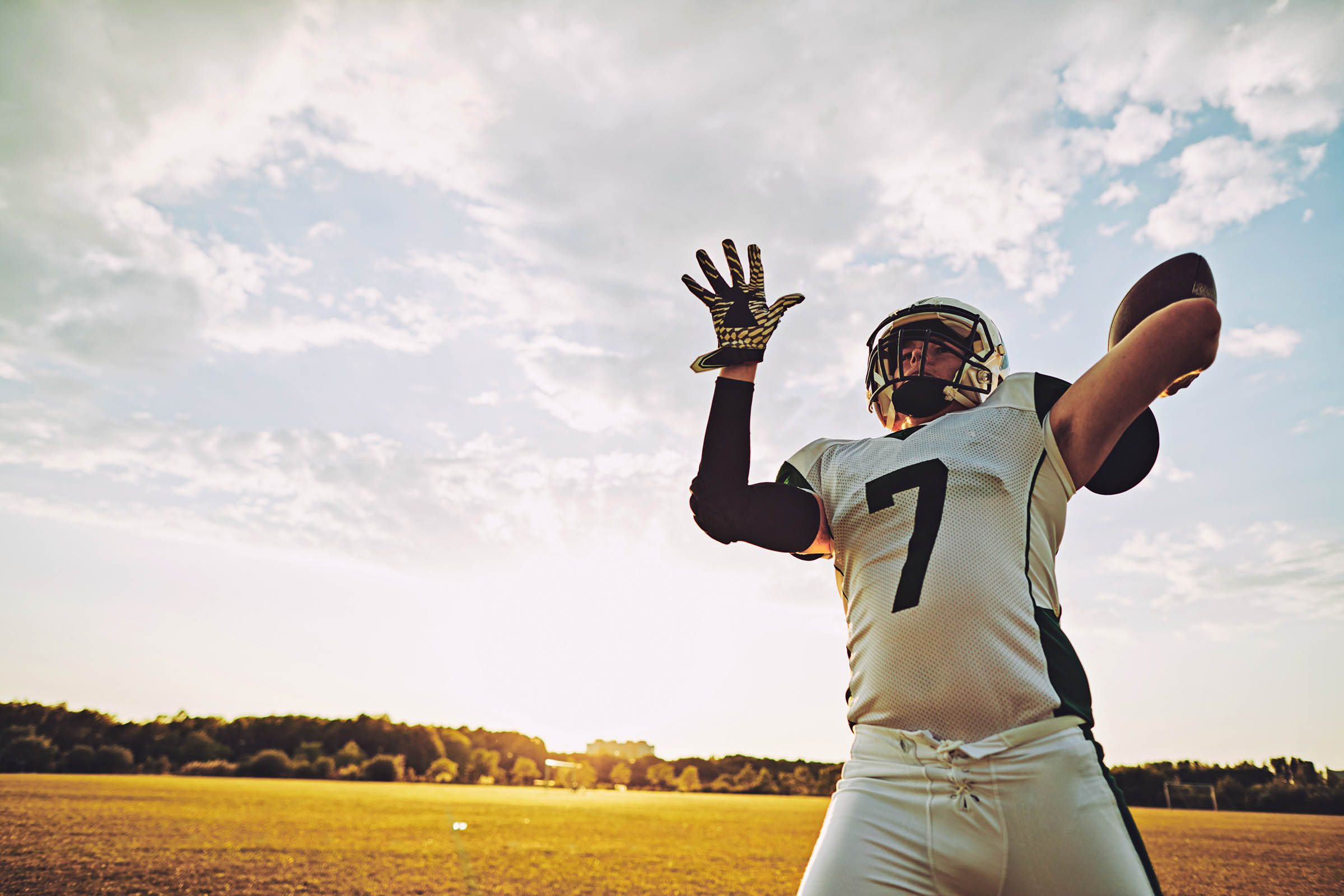 Football quarterback about to throw a pass during team practice with clouds in background