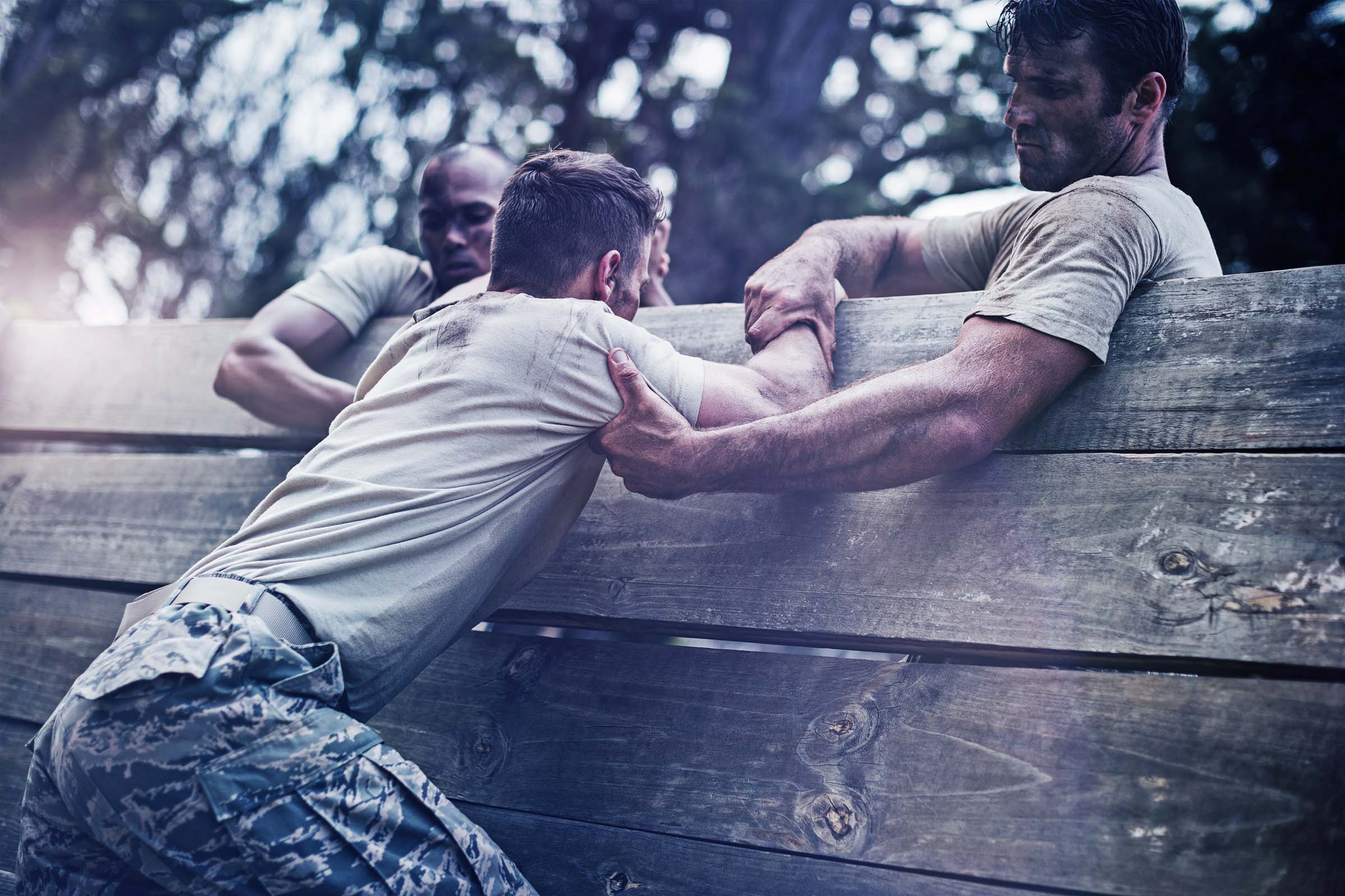 Soldiers helping man to climb wooden wall