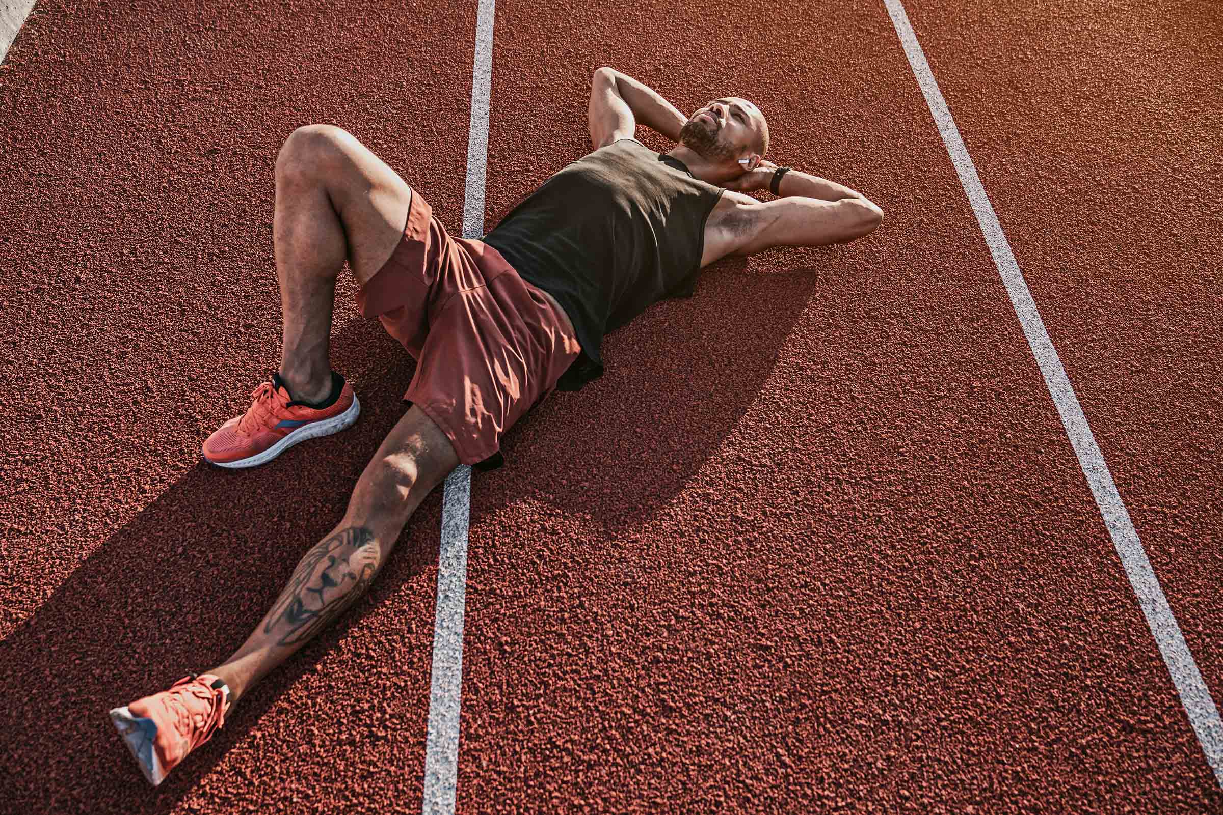 Runner lying on the track resting after workout Soldiers helping man to climb wooden wall