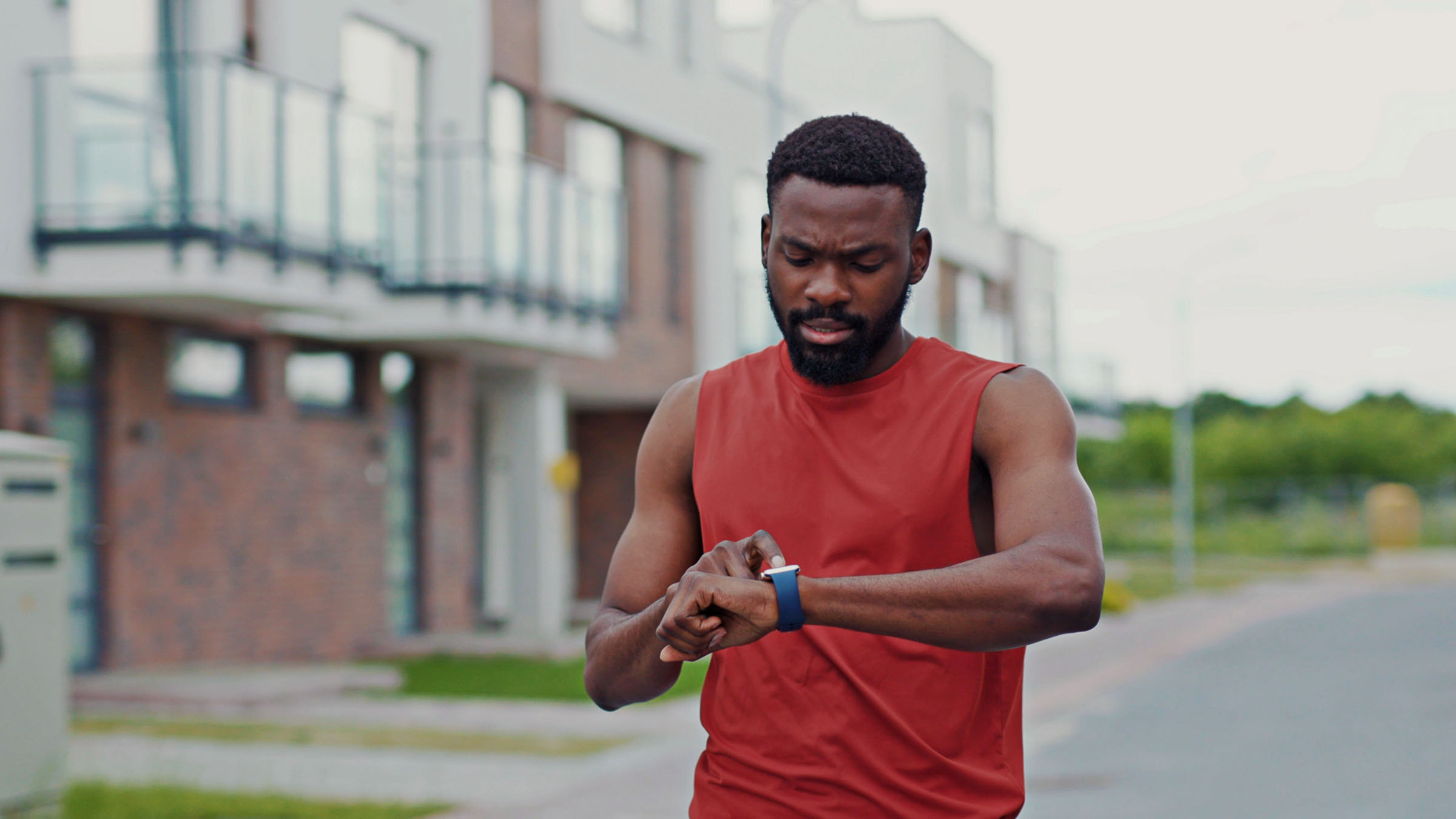 Man running in the street looking on heart rate monitor on smartwatch. Portrait of motivated athlete using fitness tracker training outdoors.