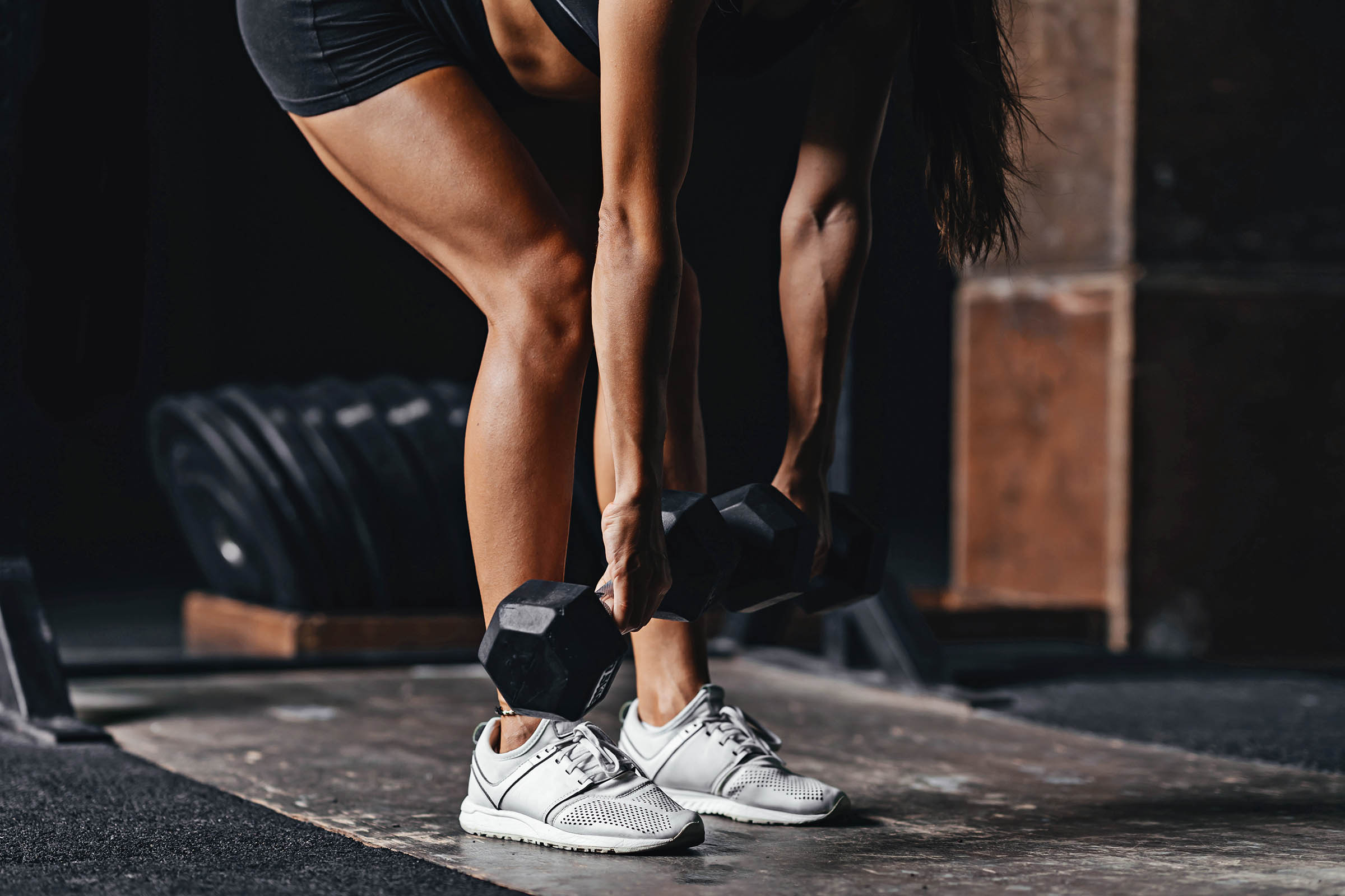 Young woman performing a Romanian deadlift at a crossfit style gym on dark gray background.