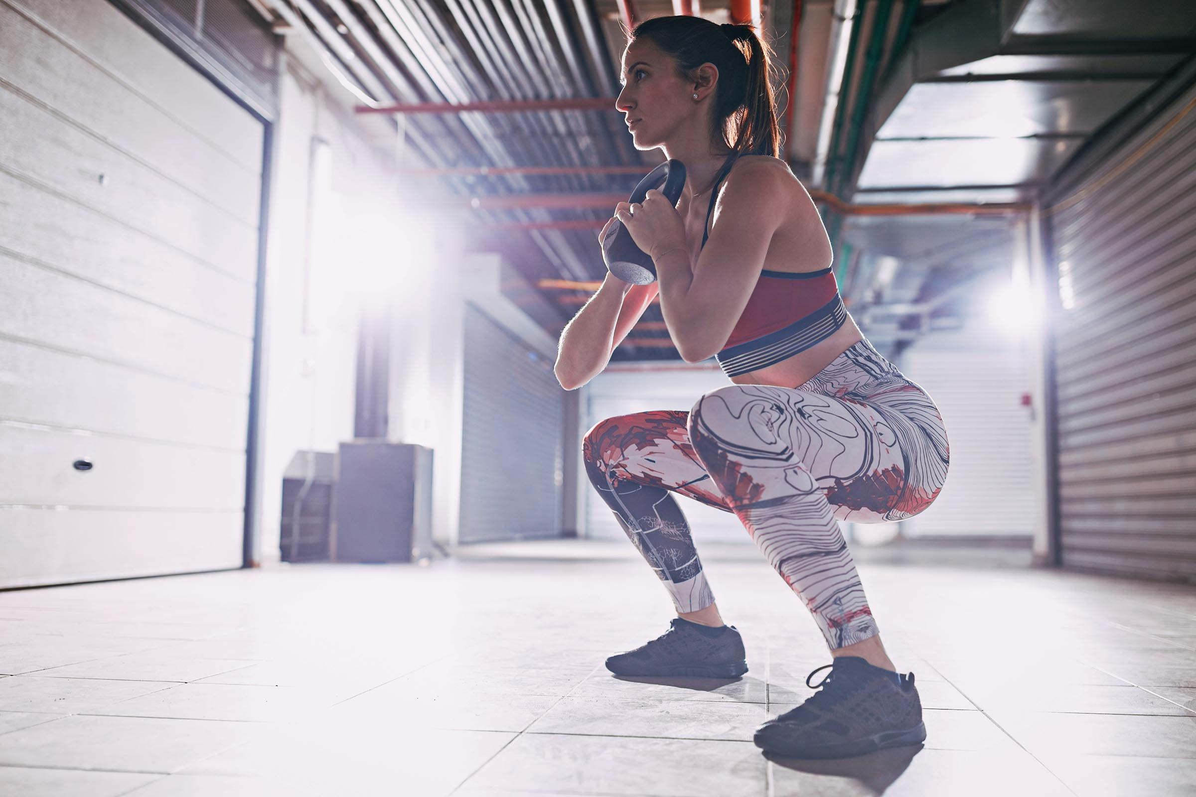 Young muscular woman exercise goblet squat with kettlebell on hard training at the garage gym.