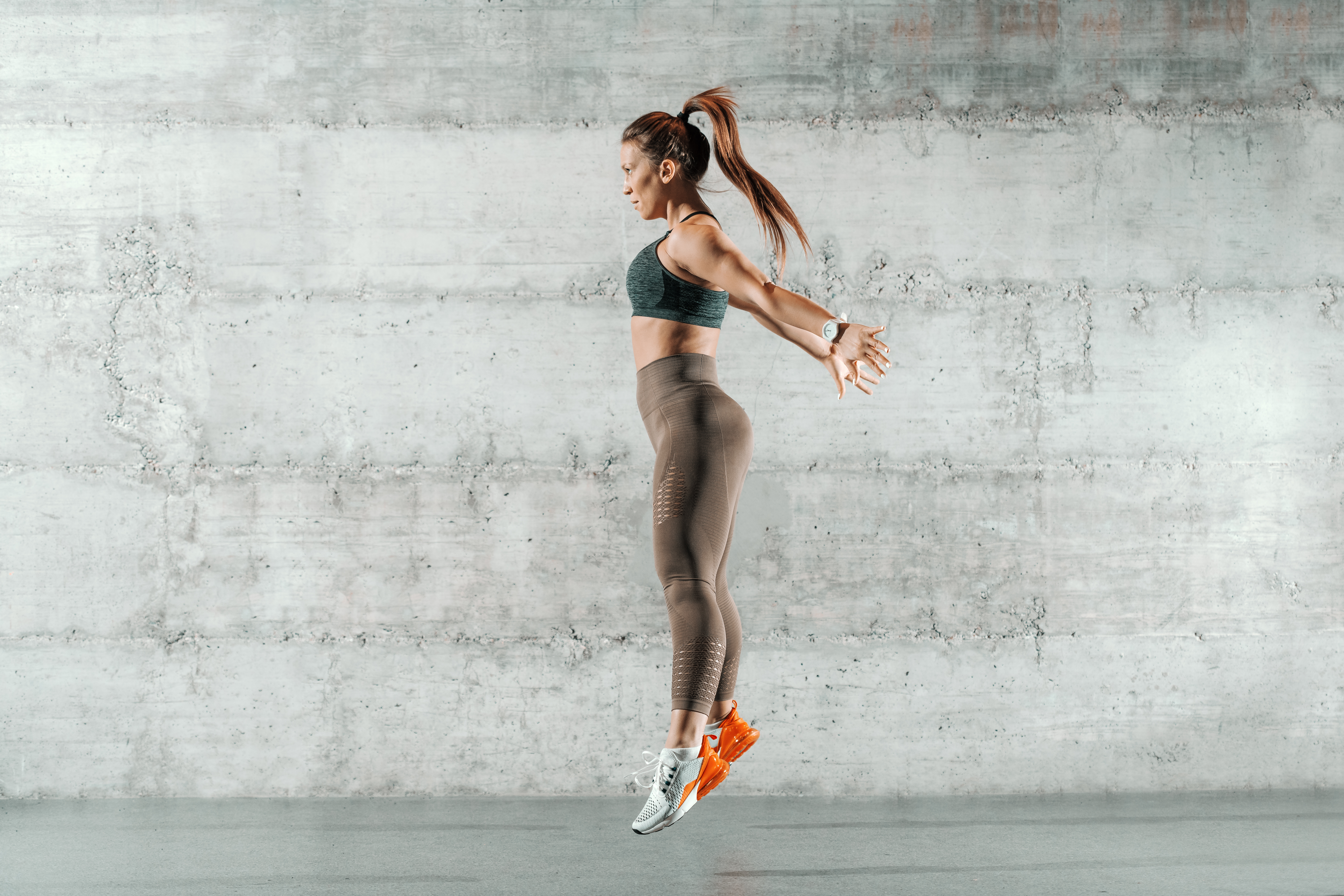 Sporty woman doing plyometric exercise jump in front of a white wall