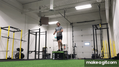 Man doing a double leg depth drop from a plyometric box on turf in a gym