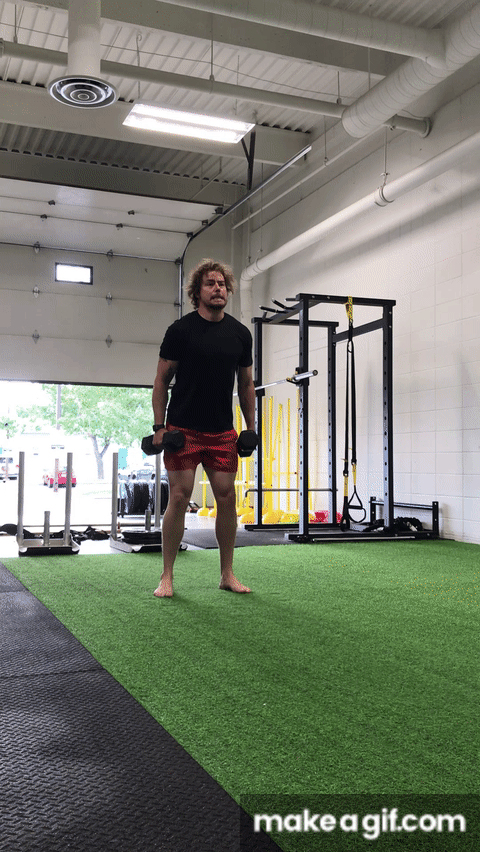Man doing loaded squat jump with dumbbells on indoor turf field gym