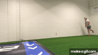 Man doing a single leg hop and landing on one foot on indoor turf field with solid white background