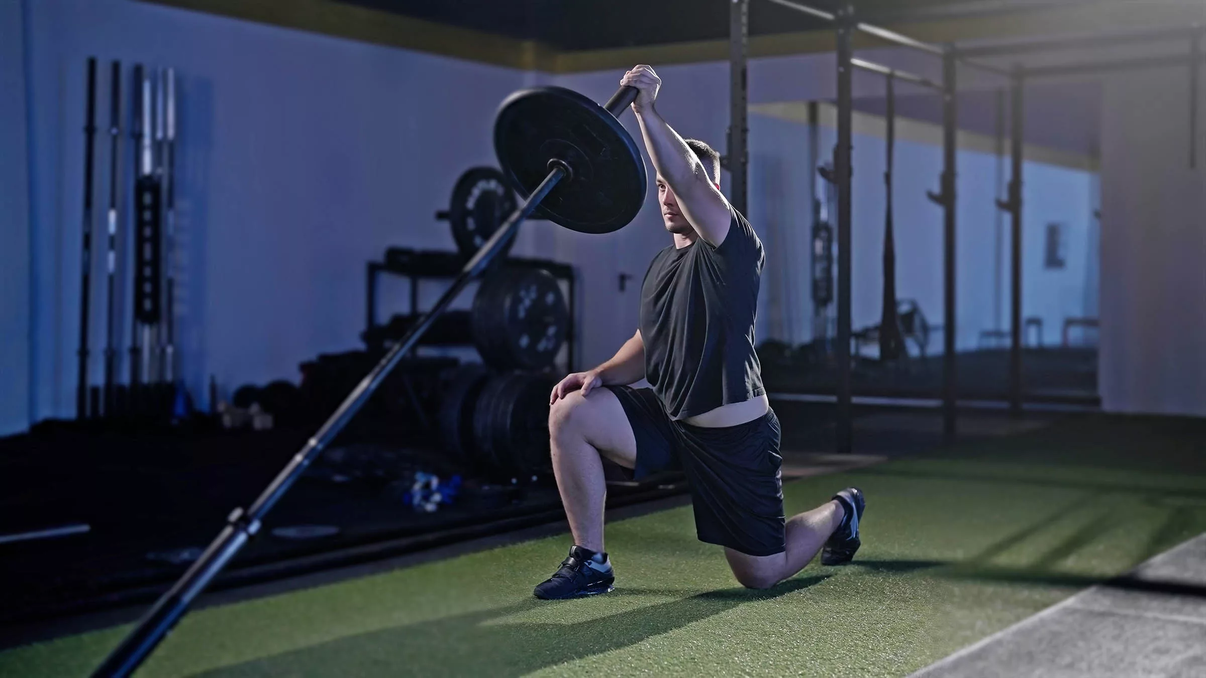 Fitness man performing landmine exercise with barbell while kneeling down in a gym