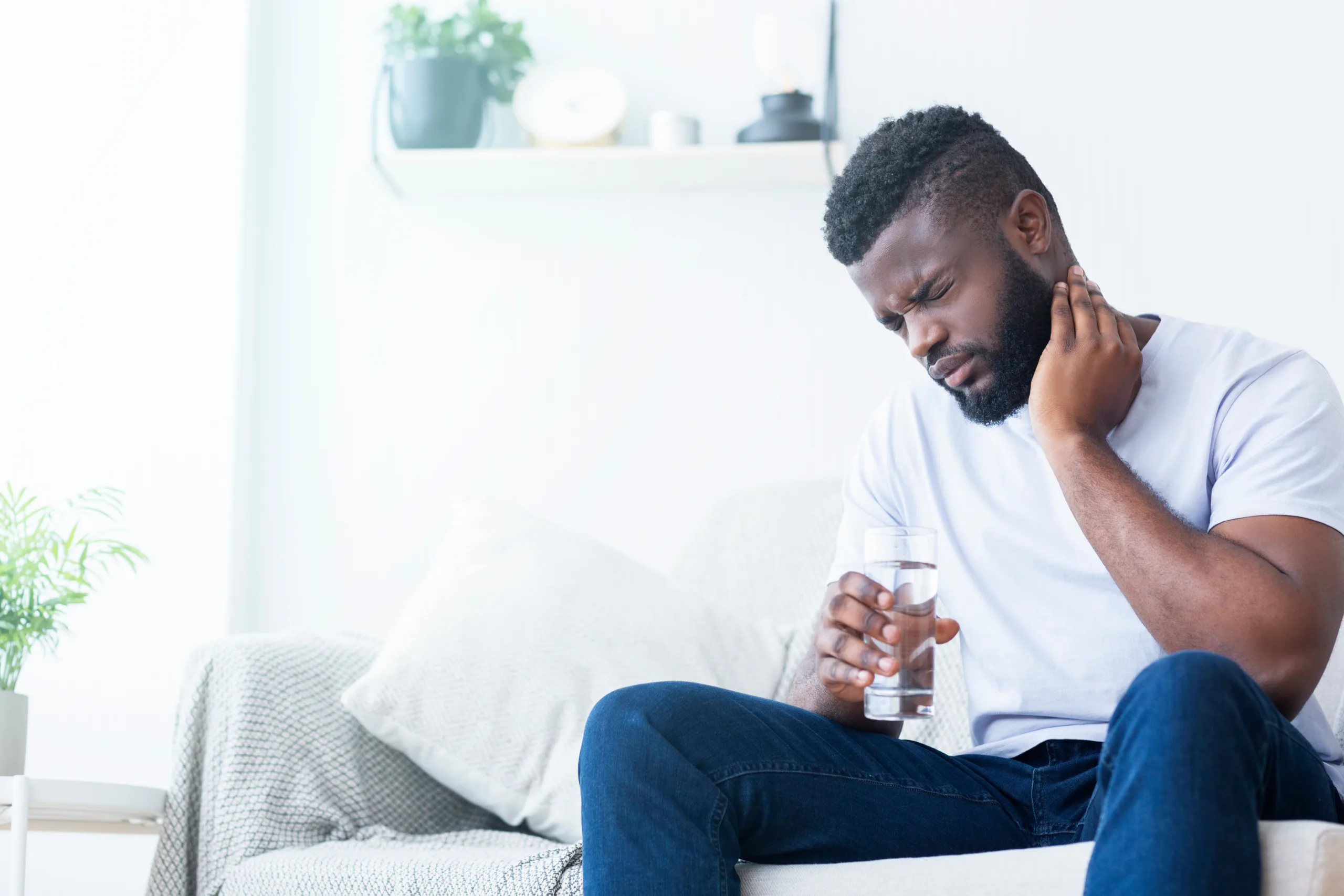 African American man suffering from neck pain, grimacing at home