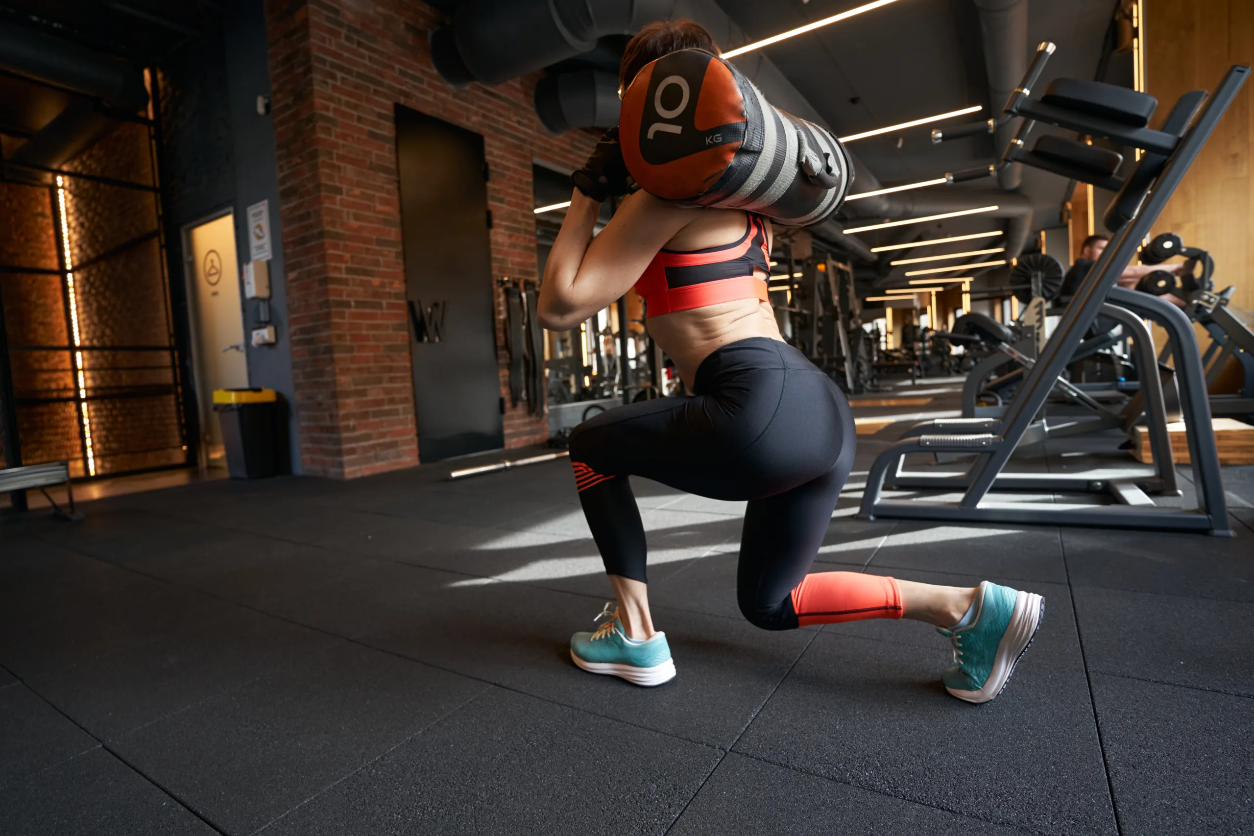 Professional female athlete performing forward lunge exercise with sandbag over shoulders