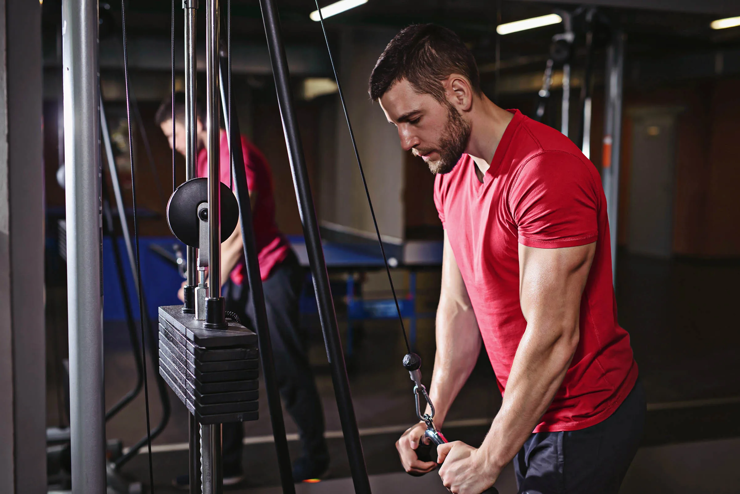Man in gym wearing red shirt doing triceps extensions for bigger arms on the cable machine