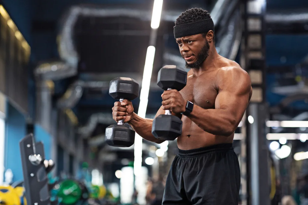 Shirtless man in gym doing hammer curls with two dumbbells for stronger, bigger biceps.