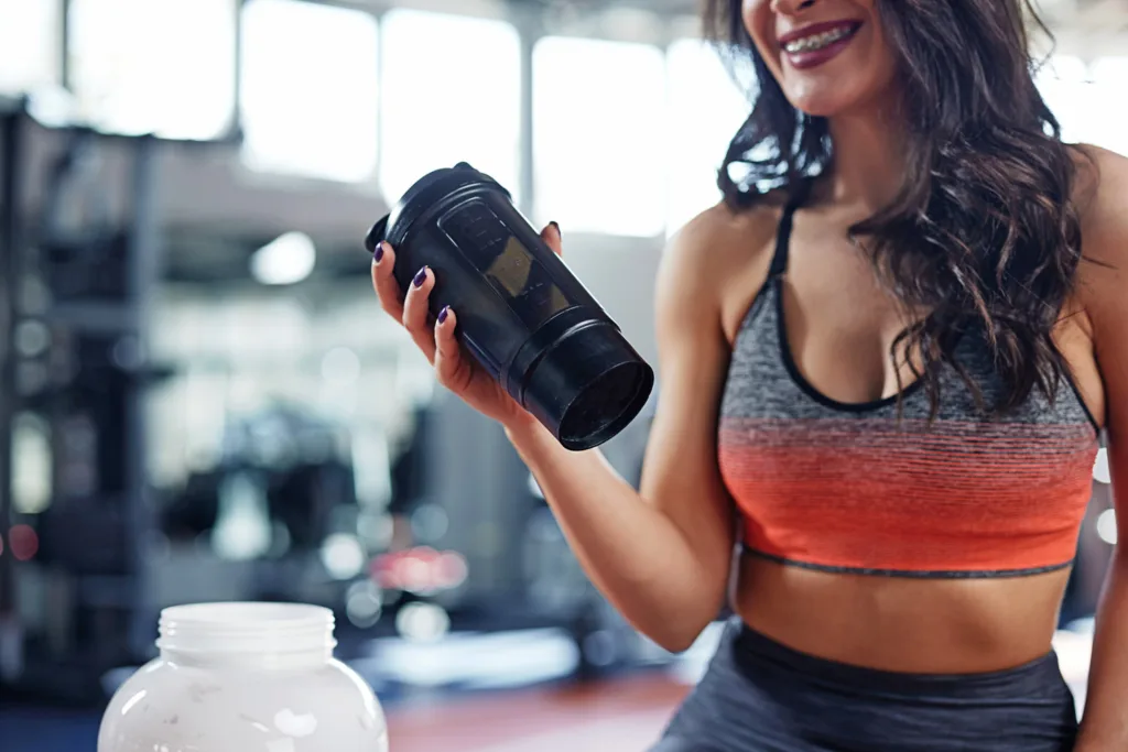 Young active woman taking a break in the gym and drinking protei