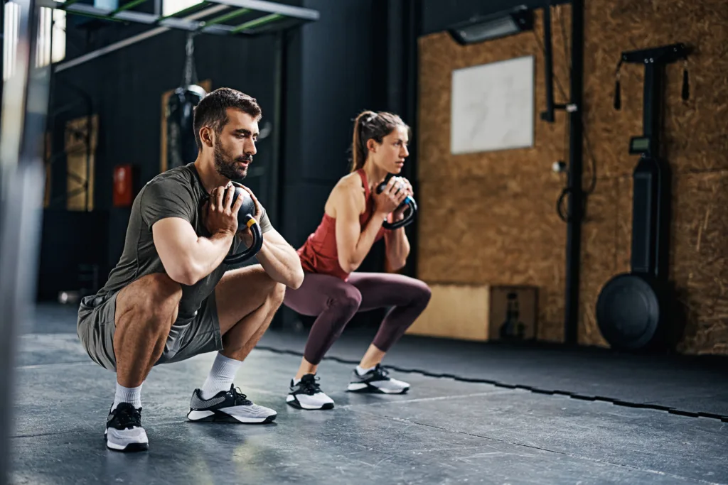 Athletic couple doing kettlebell goblet squat exercise during cross training in gym.
