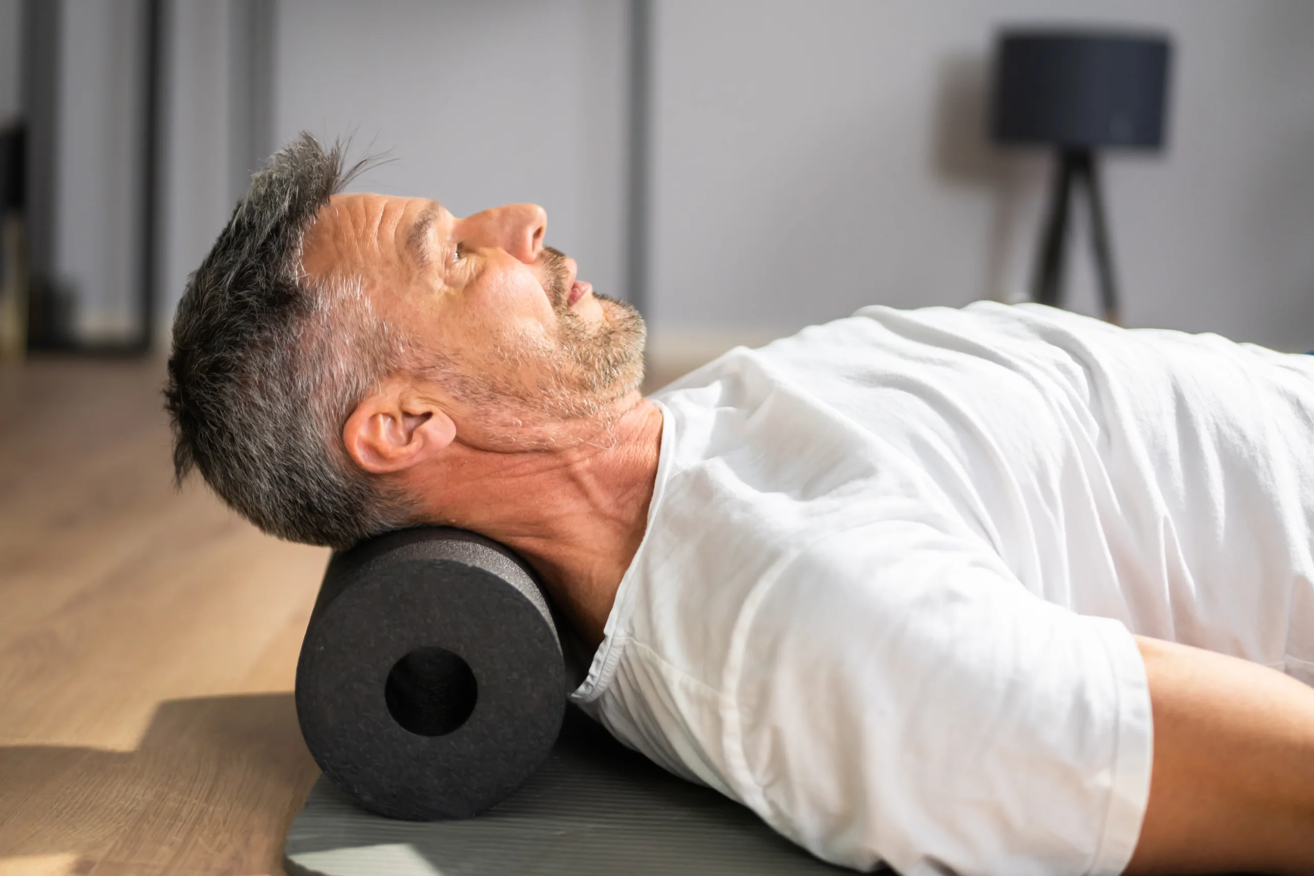 Close up of man lying flat on his back with a foam roller under his neck supporting his neck