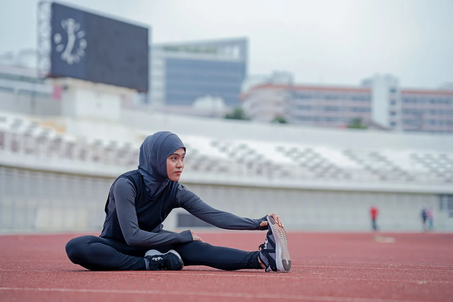 Female Muslim athlete stretches on the track while sitting down wearing a Hijab