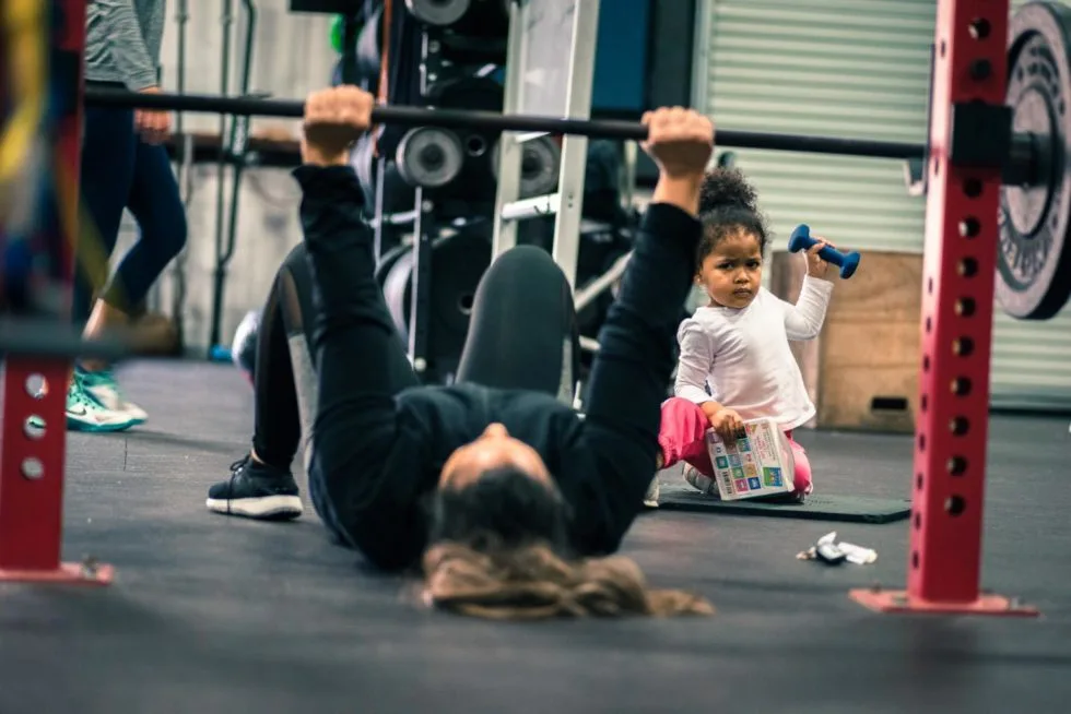 Fit mom doing floor press with her child watching
