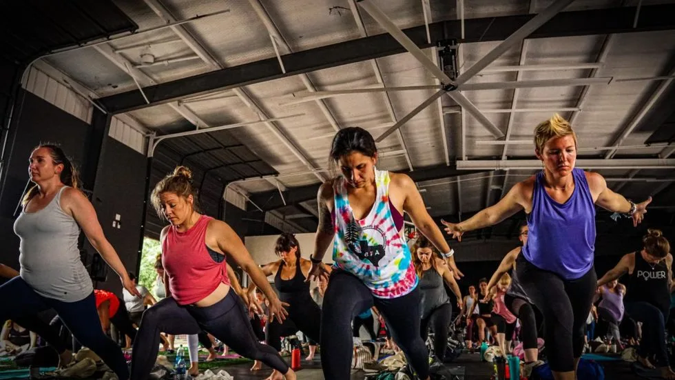 Four women in tank tops and workout clothes doing lunges in a gym