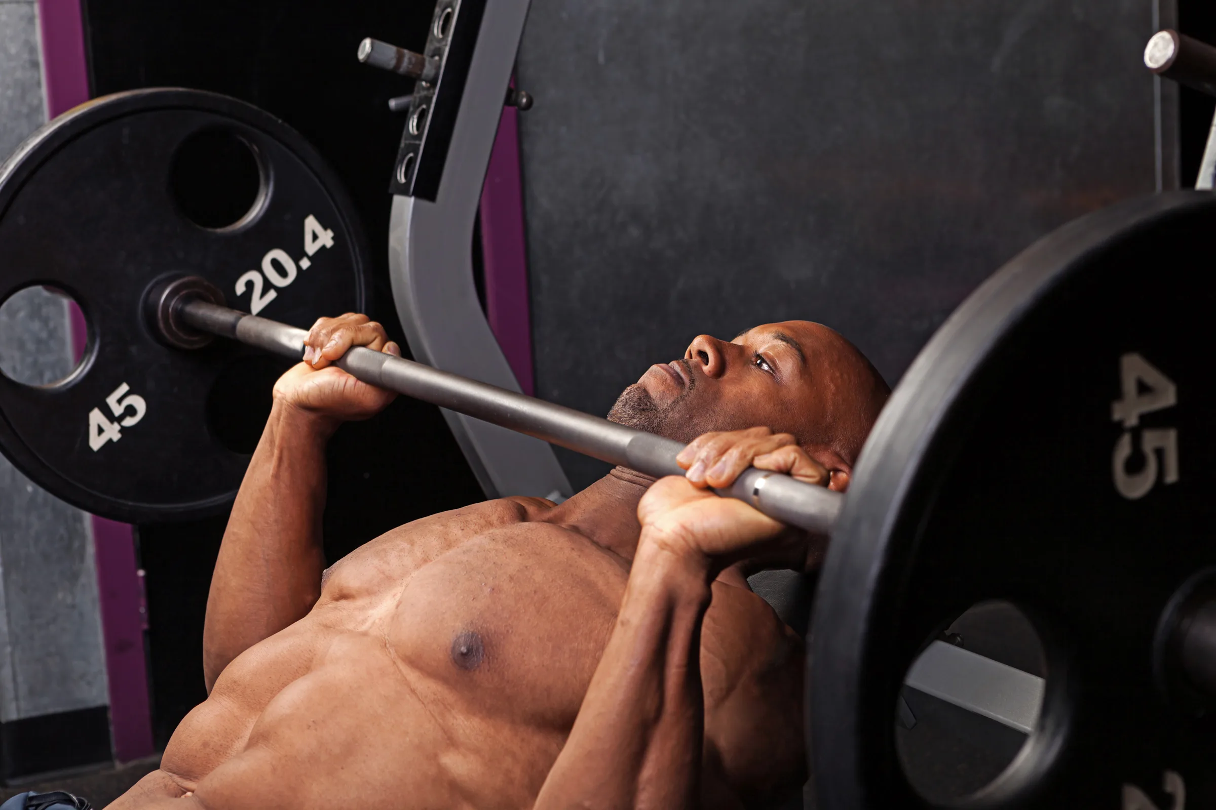 Professional athlete sits with a barbell on his shoulders and prepares to back squat. View from the back.