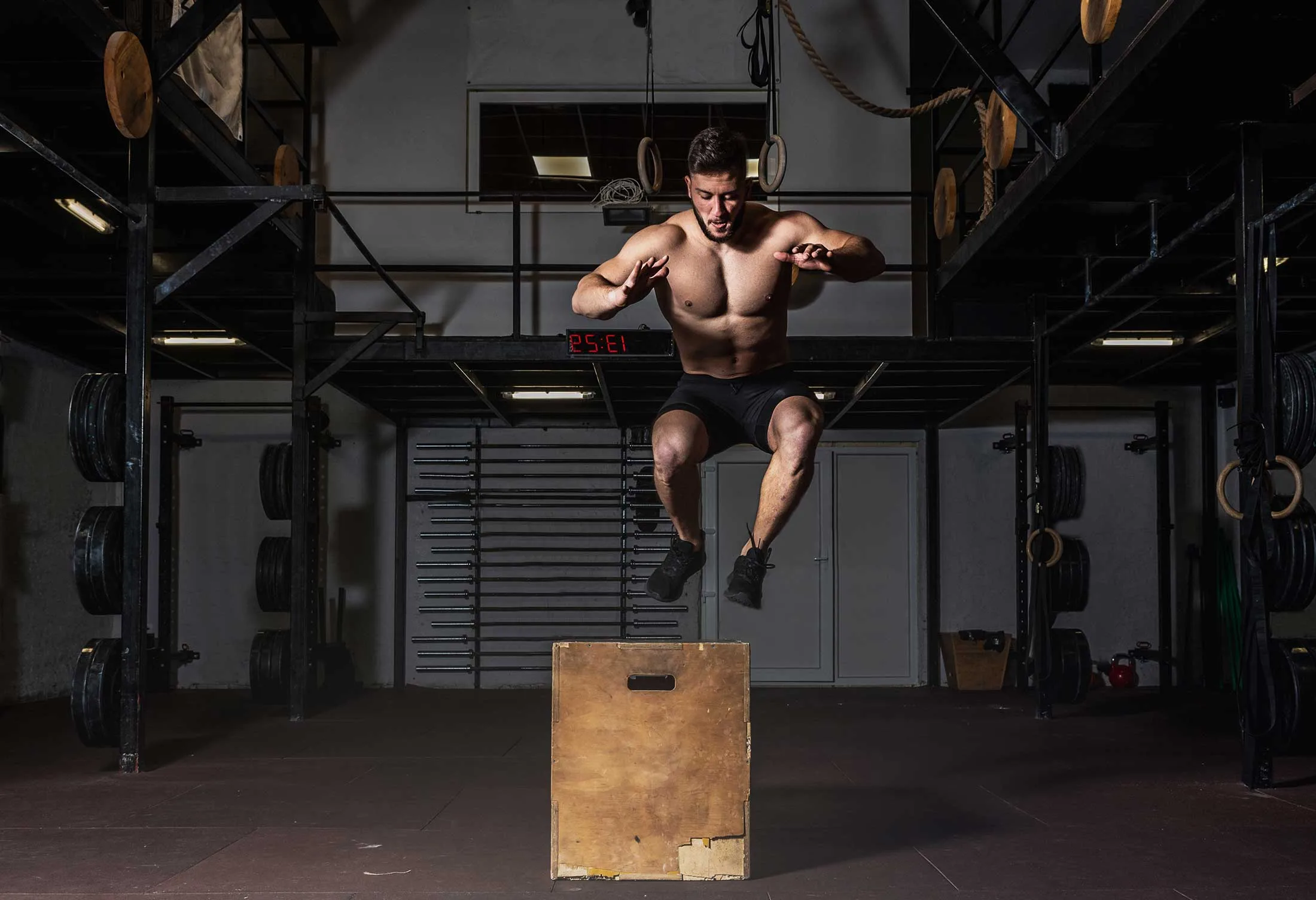 Young active strong shirtless sweaty fit muscular man with big muscles doing box jump hardcore workout training in the gym real people