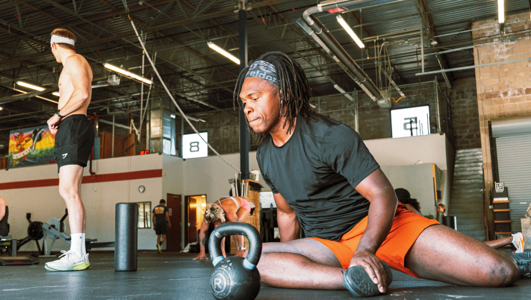 Male athlete on ground of gym stretching body as part of warm up for training session