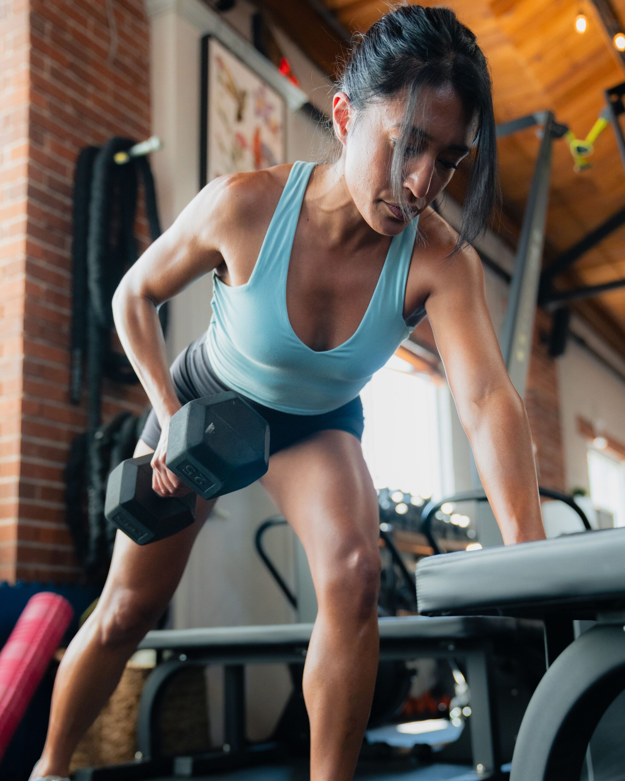 Female athlete performing single arm row with dummbell in gym